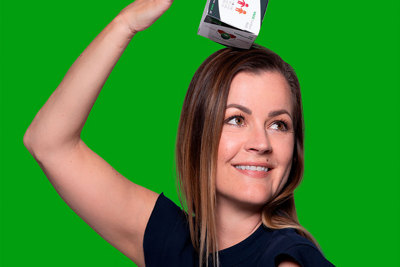 junge Frau hält einen VACE Papier Würfel auf dem Kopf grüner Hintergrund