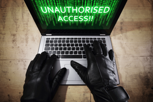Laptop auf dessen Screen die Worte 'unauthorised access' steht und jemand mit schwarzen Handschuhen an, der den Laptop hacked 