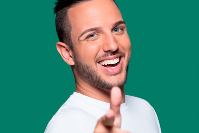 junger Mann zeigt mit grinsendem Gesicht mit dem Finger nach vorne grüner Hintergrund