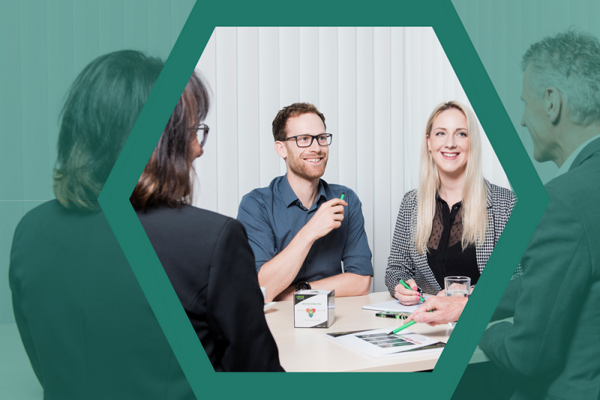 4 Personen am Besprechungstisch - mit grünem Hexagonrahmen 
